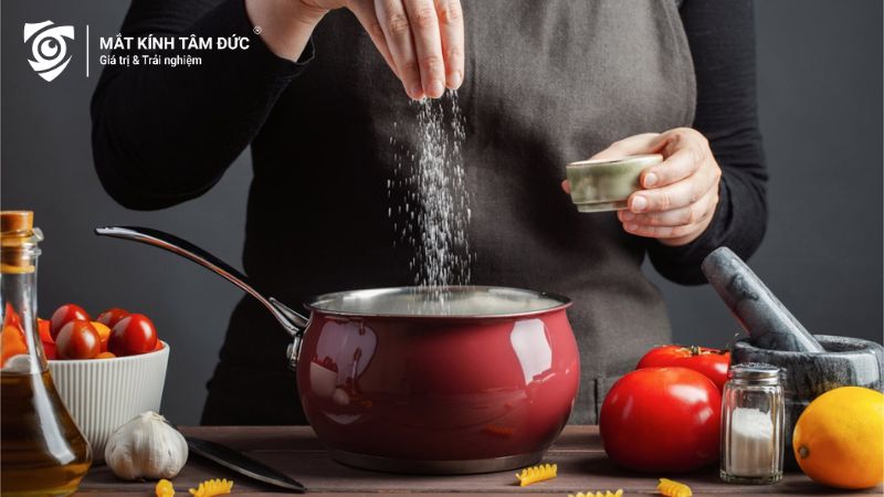 Đầu bếp đang rắc muối vào nồi khi nấu ăn, một yếu tố có thể gây tích nước trong cơ thể, làm sưng mắt sau khi khóc