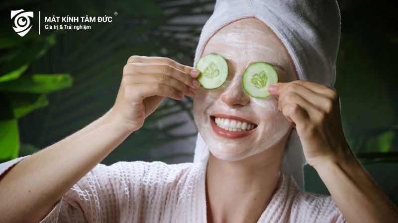 Người phụ nữ thư giãn với mặt nạ và đặt lát dưa leo lên mắt để làm dịu vùng da xung quanh.