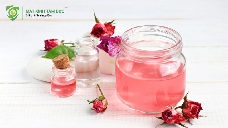 Hũ nước hoa hồng tự nhiên với cánh hoa hồng khô xung quanh, giúp giảm sưng mắt.