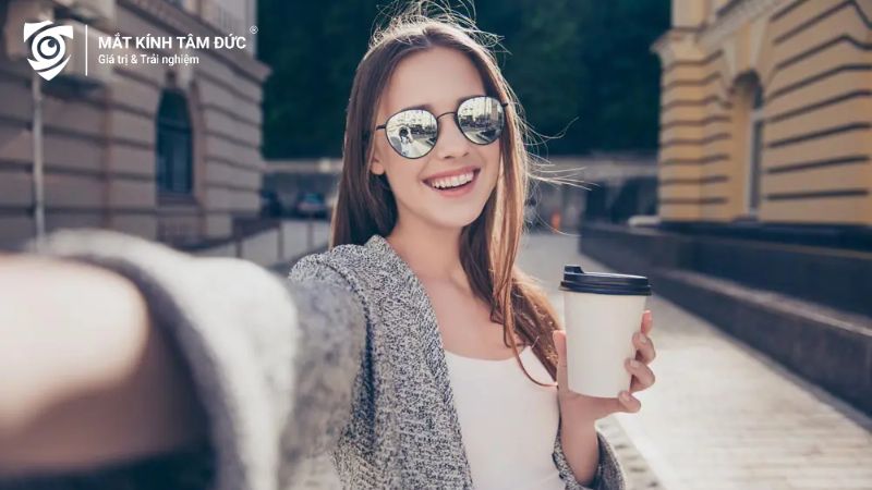 Cô gái đeo kính mát đang cầm cốc cà phê màu trắng và selfie