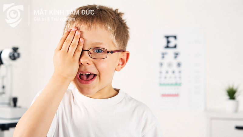 Bé trai đeo kính che một mắt khi kiểm tra thị lực cho tròng kính kiểm soát cận thị
