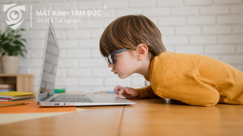 Bé học sinh đeo kính ngồi sử dụng thiết bị điện tử